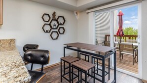 A modern kitchen with granite countertops, a black leather bar stool, a wooden dining table with black metal legs, and hexagonal wall decor. - Mountain View Haven - Luxe Townhouse with King Suite & Warm Garage (Wasilla)
