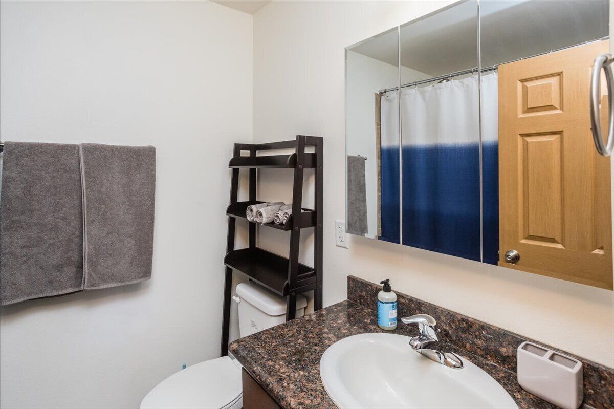 A bathroom with a double sink, a towel rack with towels, a mirror, and a shower curtain.