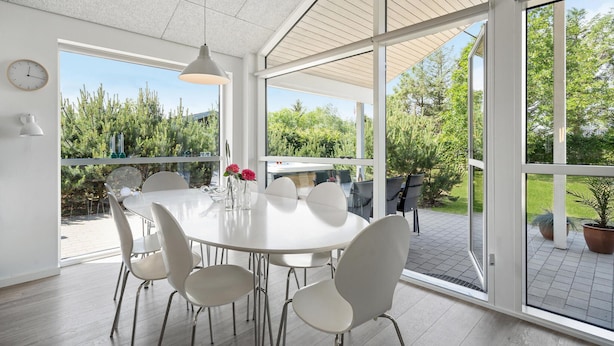 A spacious room with a large dining table and chairs, a hanging light fixture, and a view of a garden through large windows. - Gorgeous home in Tarm with WiFi (Tarm)