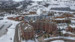 Estância coberta de neve com edifícios de vários andares, área de piscina central e montanhas ao fundo.