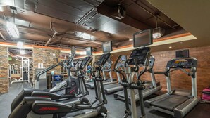 Ginásio com várias máquinas de cardio, incluindo elípticas e esteiras, e uma área de musculação ao fundo.