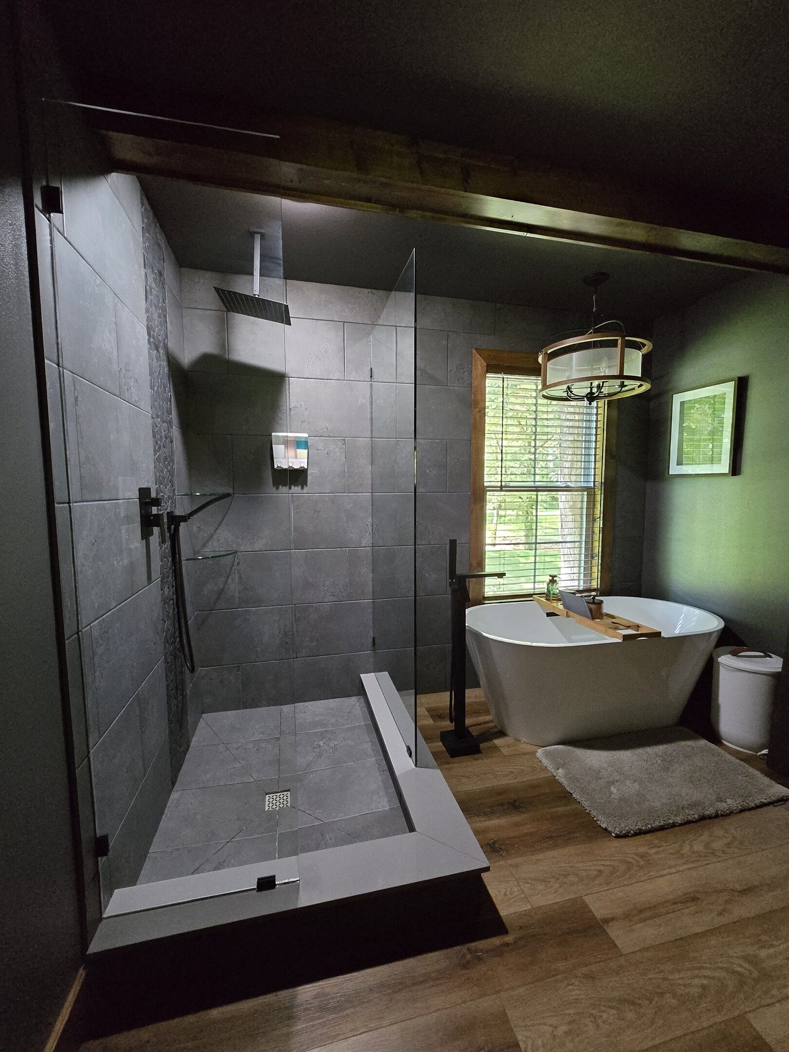 Un baño moderno con ducha de vidrio, una bañera independiente y una ventana con persianas.