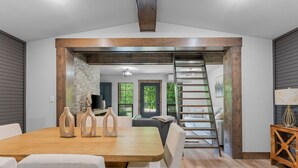 A modern dining area with a wooden table and chairs, a stone wall, and a view of the outdoors. - Creek Swimming Boulder Hot Tub Close Buffalo River (Marshall)
