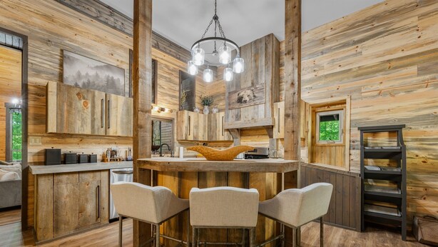 A rustic kitchen with wooden walls, a central island with bar stools, and a hanging light fixture.