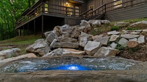 A wooden cabin with a hot tub surrounded by rocks.