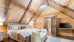 A cozy bedroom with a large bed, a white sofa, a TV, and wooden walls.