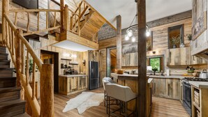 A rustic kitchen with wooden accents, a central island, and a staircase leading to an upper level.