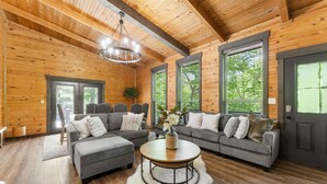 A log cabin interior with a large gray sectional sofa, a round coffee table, and a chandelier.