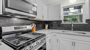 Une cuisine moderne avec des armoires blanches, un dosseret en carreaux noirs, une cuisinière en acier inoxydable et une fenêtre donnant sur les arbres.