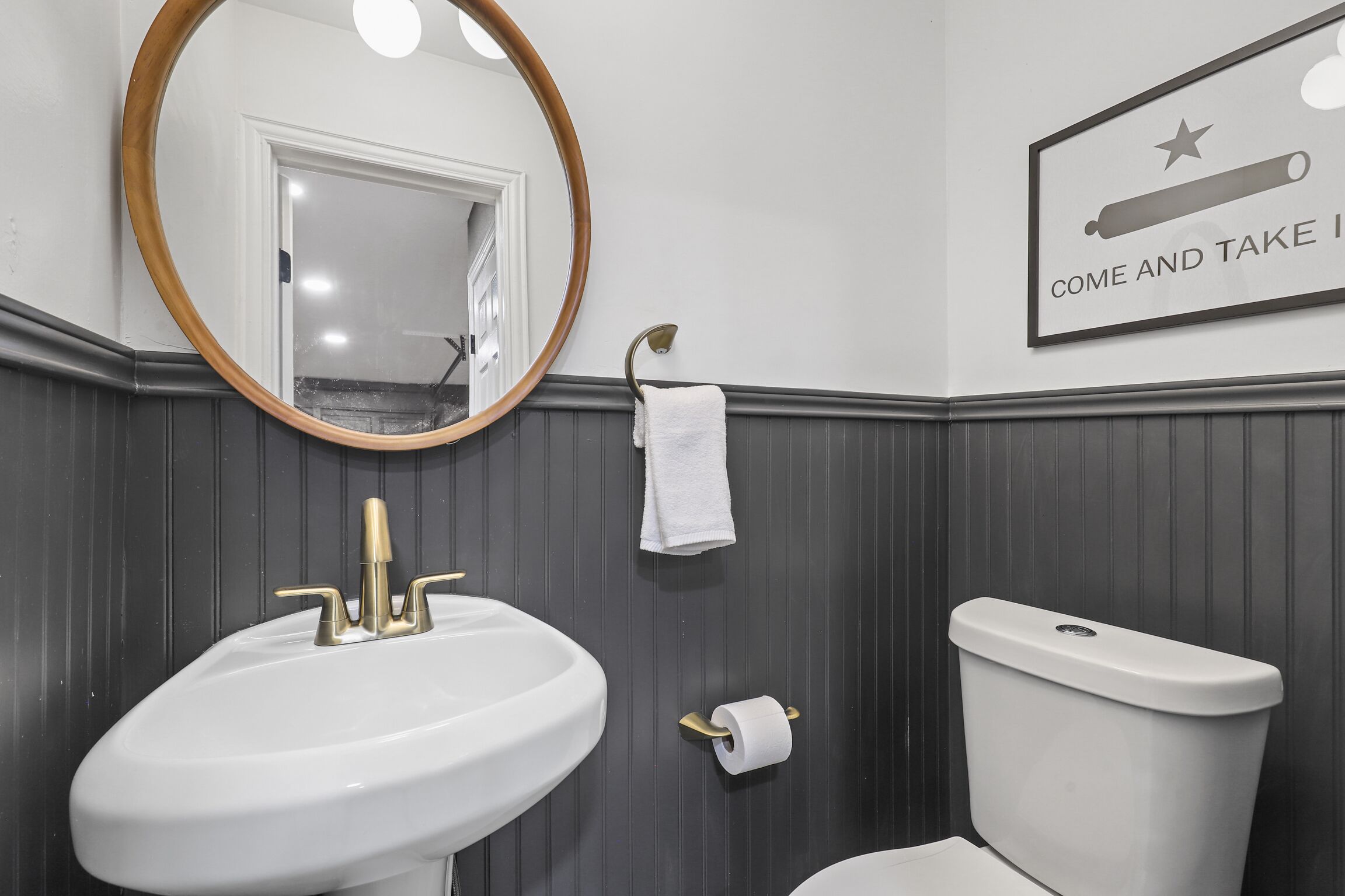 Une salle de bain avec un lavabo blanc, des toilettes, un miroir et une serviette accrochée au mur.