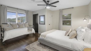 Une chambre avec deux lits, un ventilateur de plafond et de grandes fenêtres équipées de stores.