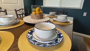 Een eettafel gedekt met wit- en blauw gemêleerde kommen, een rieten mand met fruit en placemats.