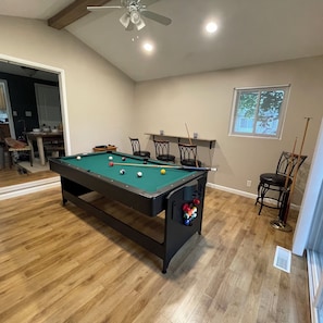 A pool table with balls, a ceiling fan, and a window with blinds.
