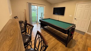 Een pooltafel in een kamer met een houten vloer, een plafondventilator en een deur.