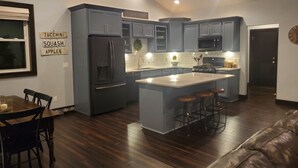 A modern kitchen with dark blue cabinets, a central island with stools, a refrigerator, and a microwave. - Residential Home 3 miles from Brennand Airport and 20 miles from EAA.  (Oshkosh)