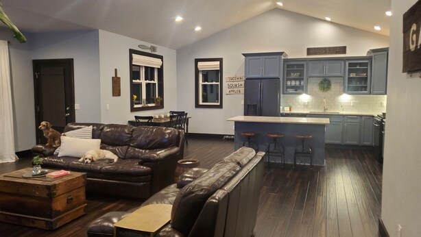 A modern living room with a leather sofa, a wooden coffee table, and a dog. There is a kitchen area with a bar stool and a refrigerator. - Residential Home 3 miles from Brennand Airport and 20 miles from EAA.  (Oshkosh)