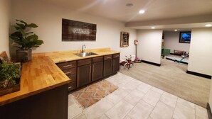 A modern kitchen with a wooden countertop, dark cabinets, and a sink. There is a potted plant on the left and a rug on the floor. - Residential Home 3 miles from Brennand Airport and 20 miles from EAA.  (Oshkosh)