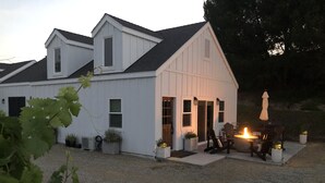 Una casa blanca con techo inclinado, un porche cubierto con mobiliario exterior y una chimenea.