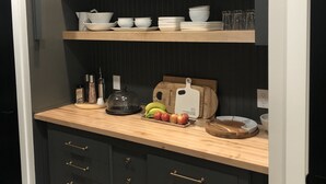 Una cocina con armarios oscuros, encimeras de madera y una estantería empotrada con platos y cuencos.