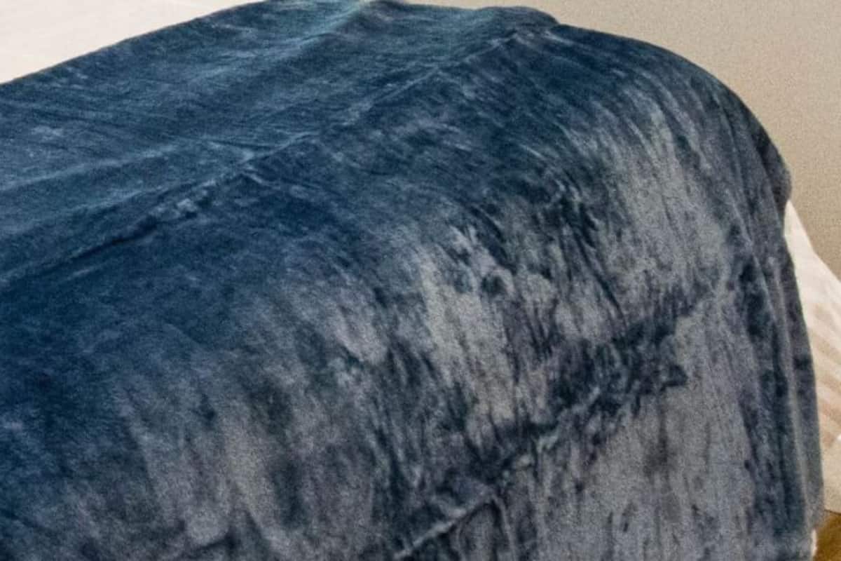 Una cama con sábana blanca y manta azul.
