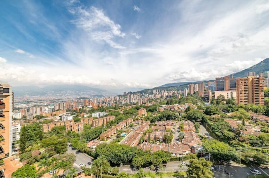 A cityscape with a mix of residential and high-rise buildings, a clear sky, and a distant mountain range.