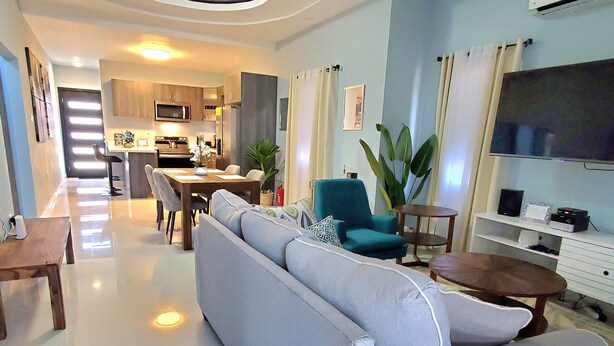 A modern living room with a sofa, a dining table, and a kitchen in the background. - Comfy Beds-Pool-Clean Getaway-2 mins to Ocho Rios (Ocho Rios)