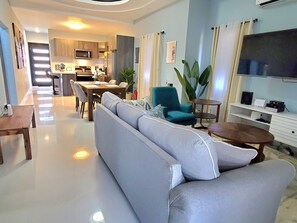 A modern living room with a sofa, a dining table, and a kitchen in the background. - Comfy Beds-Pool-Clean Getaway-2 mins to Ocho Rios (Ocho Rios)