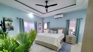 A bedroom with a bed, bedside tables, a ceiling fan, an air conditioner, and a potted plant. - Comfy Beds-Pool-Clean Getaway-2 mins to Ocho Rios (Ocho Rios)