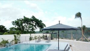 A swimming pool with lounge chairs and an umbrella, surrounded by a white wall and greenery. - Comfy Beds-Pool-Clean Getaway-2 mins to Ocho Rios (Ocho Rios)
