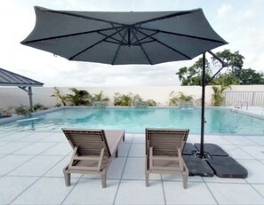 Área da piscina com duas espreguiçadeiras e um grande guarda-sol.