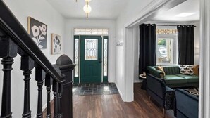 Een moderne woonkamer met een groene bank, een bijzettafeltje en een trap met zwarte leuningen die naar een groene deur leidt.