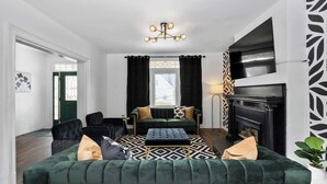 Een woonkamer met een groene bank, een zwart-wit tapijt en een open haard.