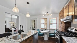 Een moderne keuken met granieten aanrechtbladen, een roestvrijstalen spoelbak en een gasfornuis. Er is een eethoek met een ronde tafel en teal-kleurige stoelen.