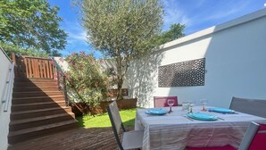Une terrasse avec une plateforme en bois, une table dressée pour deux personnes, ainsi que des chaises, et un escalier menant à un niveau supérieur.