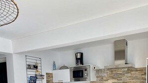 Une cuisine moderne avec des meubles blancs, un four à micro-ondes et une machine à café. On y trouve une table à manger avec des chaises et un luminaire suspendu.