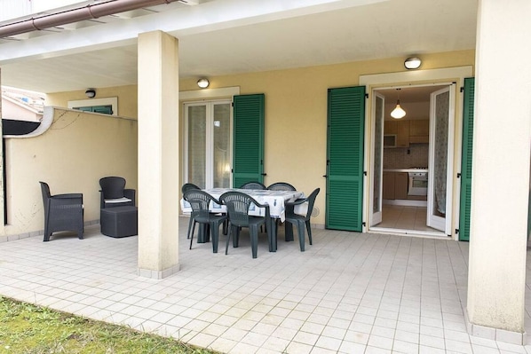 An outdoor patio with a table and chairs, a covered area, and a kitchen visible through an open door.