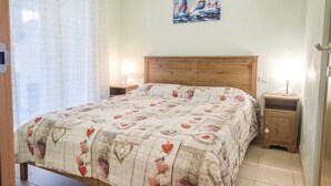 Une chambre à coucher avec une tête de lit en bois, un lit recouvert d’une courtepointe à motifs floraux, deux tables de chevet avec des lampes et un tableau accroché au mur.