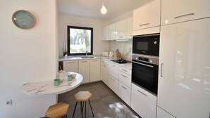 A modern kitchen with white cabinets, a built-in oven, and a round marble countertop. - Hossegor “VILLA BARRANX” Magnificent apartment for 4 people. (HOSSEGOR)