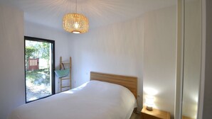 A bedroom with a large bed, a wooden nightstand, a hanging light fixture, and a view through a glass door. - Hossegor “VILLA BARRANX” Magnificent apartment for 4 people. (HOSSEGOR)