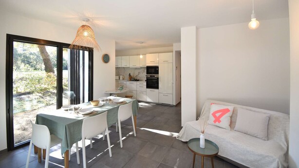 A modern kitchen with white cabinets, a dining area with a table and chairs, and a sofa with a cushion marked with the number 4. - Hossegor “VILLA BARRANX” Magnificent apartment for 4 people. (HOSSEGOR)