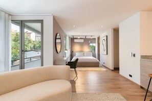 Una habitación de hotel moderna con una cama grande, una zona de estar con sofá, una mesa de comedor y vistas al exterior a través de una puerta corrediza.