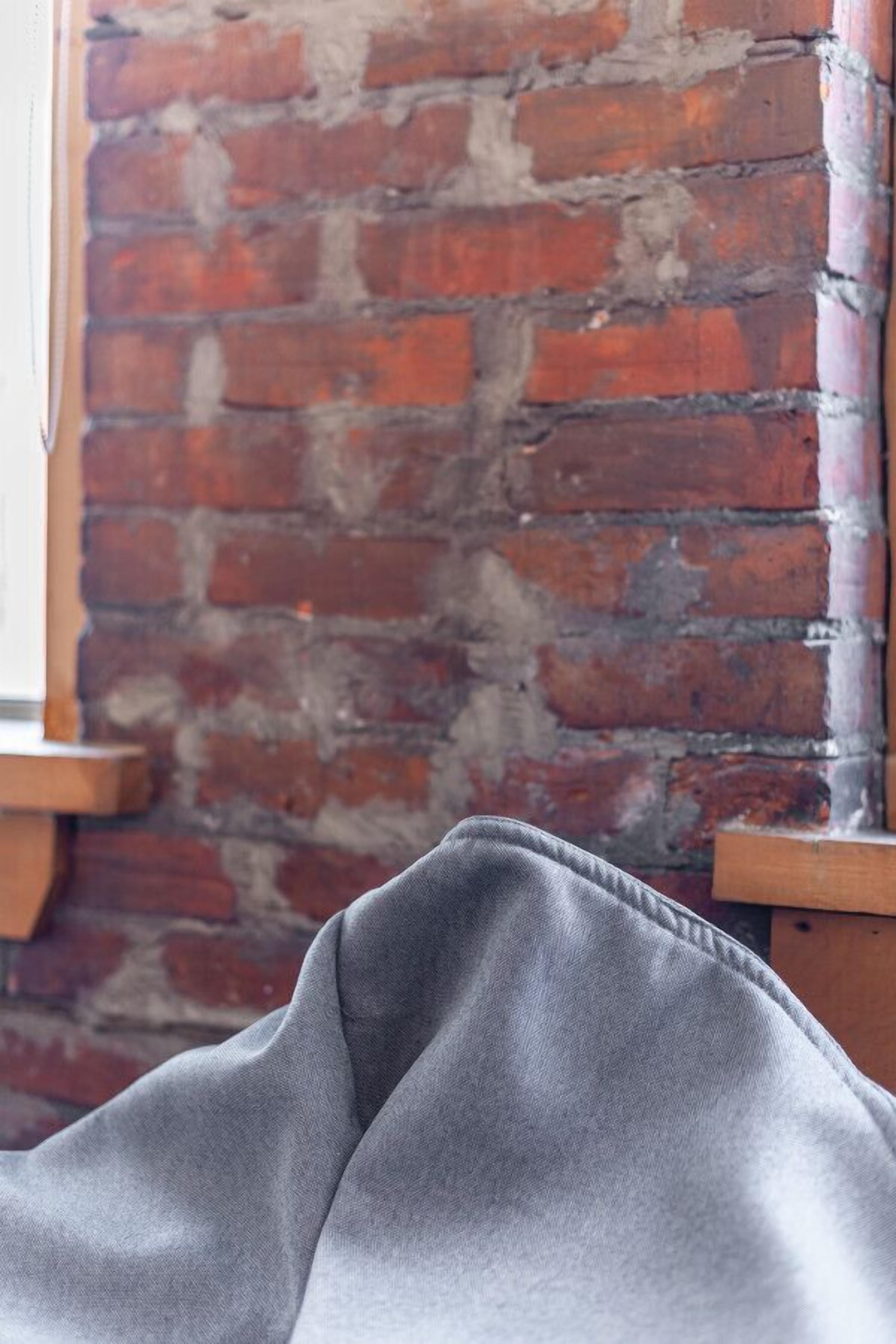 A brick wall with a wooden chair and a grey fabric item in the foreground.