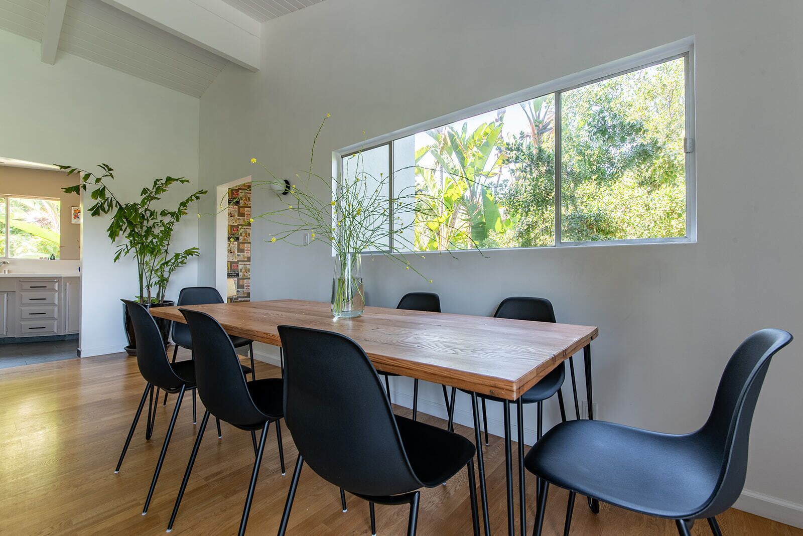 A dining area with a wooden table, black chairs, and a vase with flowers.