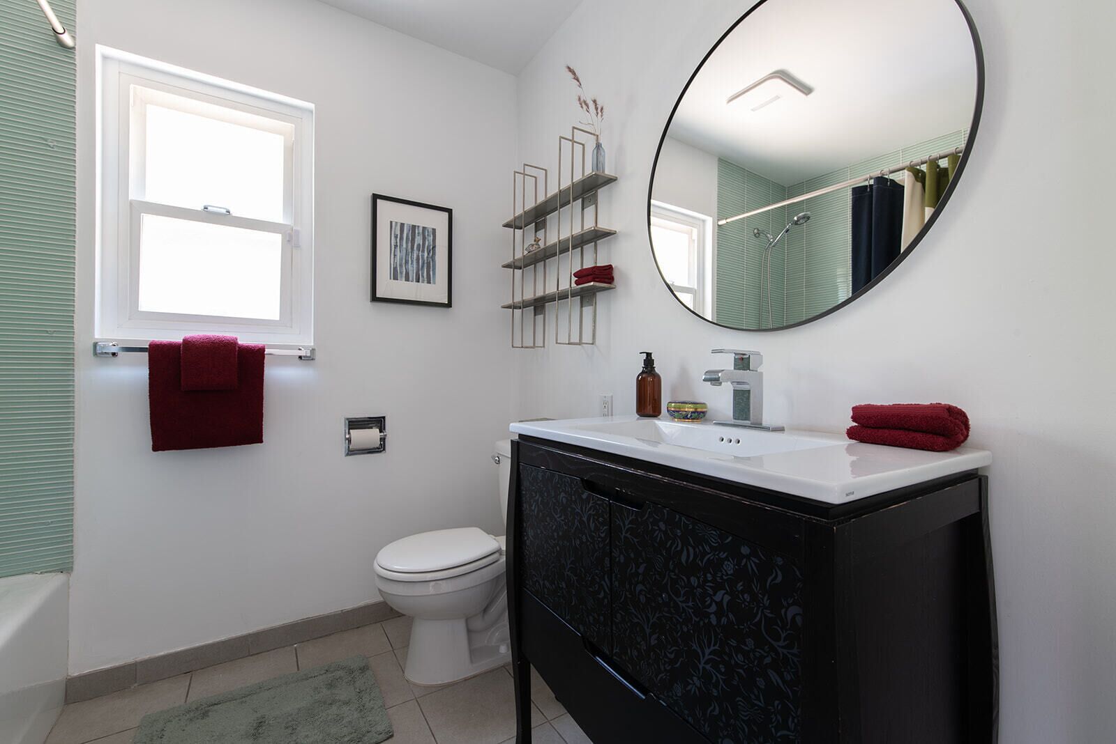 A modern bathroom with a white toilet, black vanity, and a round mirror.