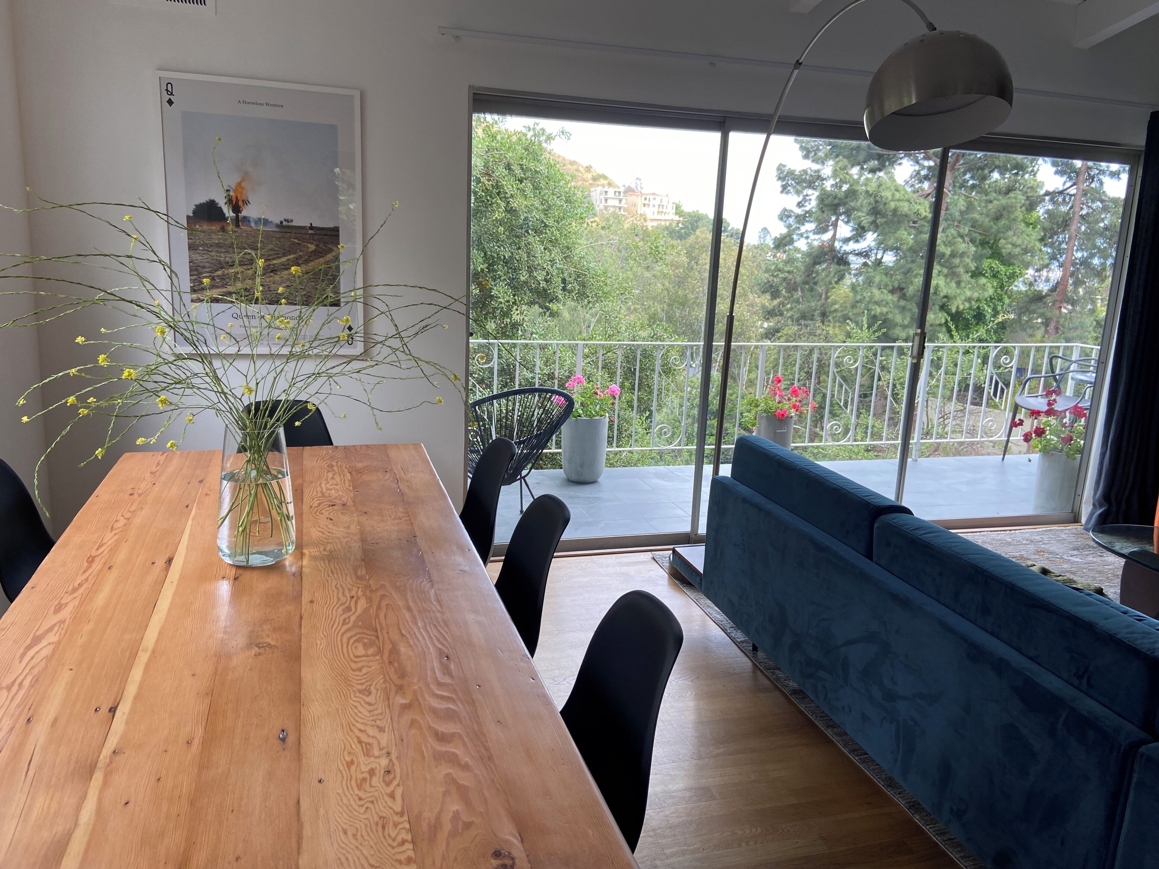 A dining area with a wooden table, black chairs, a vase with yellow flowers, and a blue sofa.