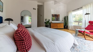 A modern bedroom with a large bed, a red chair, a dresser, and a mirror.