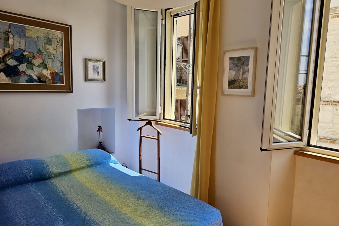 Quarto com cama, janela, quadro e uma pequena mesa.