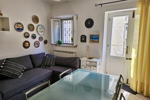 Una sala de estar con un sofá, una mesa de vidrio, una ventana con cortinas y varios adornos en las paredes.