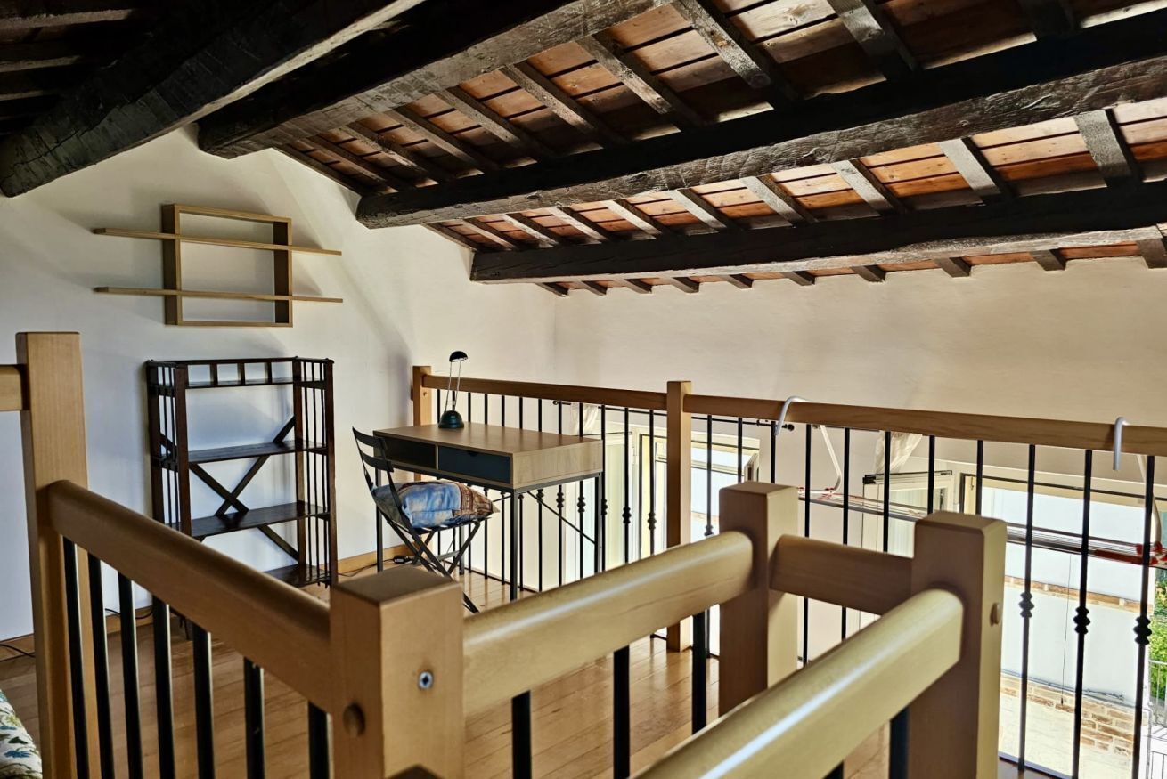 Un escalier en bois avec une rampe, une petite table avec une chaise et une fenêtre donnant sur un beau paysage.