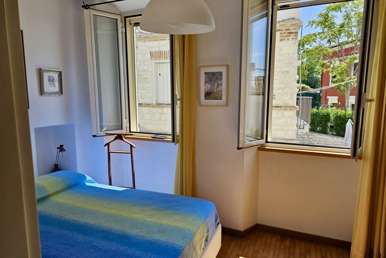 Ein Schlafzimmer mit Bett, zwei Fenstern und Blick nach draußen.